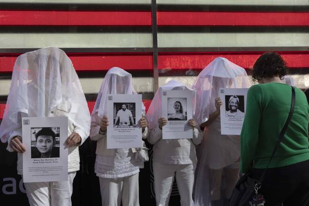 October 25, 2026, New York, New York, USA: A passerby stops to observe people dressed in white shrouds, Human Beings, memorializing those killed by gun violence from Federal immigration agents by holding signs with the images and names of Ruben Ray Martinez Lorenzo Salgado Araujo Renee Nicole Good Keith Porter Jr. Demonstrators with the anti-gun violence organization Gays Against Guns protest under the Times Square US Army Recruiting Station LED American flag to denounce U.S. Immigration and Customs Enforcement (ICE,) President Trump s immigrant detention and mass deportation policies. New York USA - ZUMAr174 20261025_znp_r174_012 Copyright: xGinaxMxRandazzox