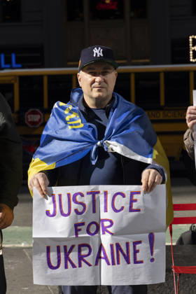 October 25, 2026, New York, New York, USA: A demonstrator wears a Ukrainian flag tied over his shoulders and holds a sign that reads JUSTICE FOR UKRAINE! while standing with a group of protesters in Times Square. New York USA - ZUMAr174 20261025_znp_r174_026 Copyright: xGinaxMxRandazzox